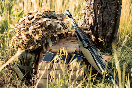 A military helmet, a military machine gun, and a backpack lie piled up on the grass near a tree. Preparing things for battleの写真素材
