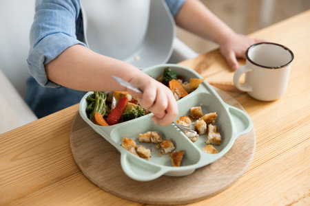 Top view of how a toddler boy pricking food with a fork from a special childrens plate. Concept of self-feeding. BLW. Child without the help of adults eats healthy vegetables with meat. close-upの写真素材