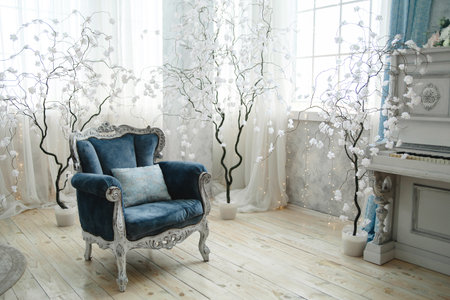 Luxurious blue velvet armchair set against a backdrop of white decorative trees and soft, ambient lighting. Ideal for promoting high-end interior design and home decor eleganceの写真素材