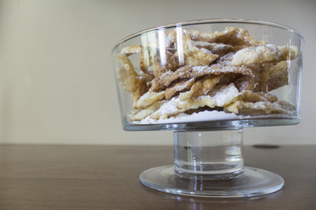 Sprinkle with powdered sugar, fried plate of shortcake dough. Dessert Polish and Lithuanian cuisine - faworki (angel wings). Faworki in a large glass vase on a beige background.の写真素材