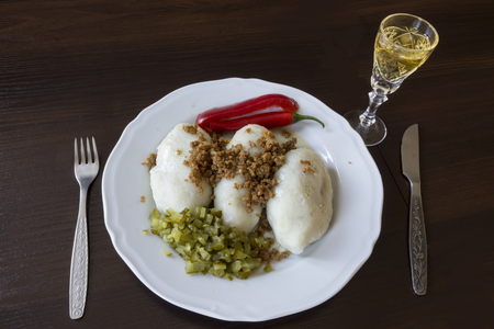 Potato dumplings - a traditional regional dish. Polish and Lithuanian cuisine. With pickles, fried bacon and paprika. White plate, knife, fork and glass of vodka on a dark background.の写真素材
