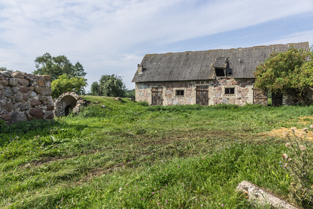 The farmyard is an agricultural abandoned farm. The old collapsed barns. The entrance to the cellar is like a cave. The end of the summer . Podlasie, Poland.の写真素材