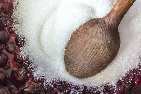 Cooking cherry jam . Hot dark red cherries, white granulated sugar and a wooden spoon. Site about fruits, berries, food, cuisine and cooking.の写真素材