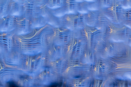 Macro photo. Abstract background . Twisted reflections of a multistory building in violet drops of water. Yellow blurred lines of lamps and lanterns.の写真素材