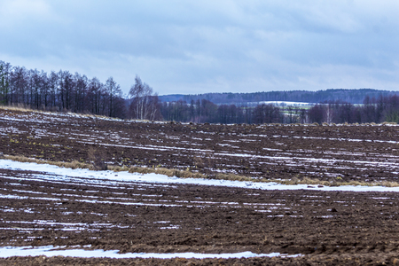 On the plowed field lies a bit of snow. Dark forest surrounds the fields. The beginning of winter in Europe.の写真素材