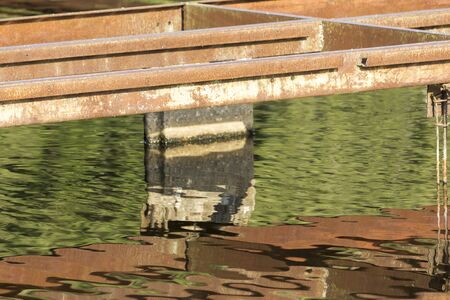 Old rusty metallic boat pier on a lake in a park. Site about metal, park, boat, recreation, reconstruction, metal corrosion.の写真素材