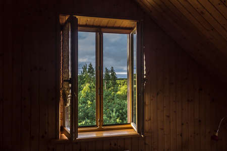 Summer in the village. Early morning. Scenic view from the window to the sky and trees. Room in the attic, with wooden siding.の写真素材