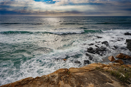 Sun rays shining through the clouds of a  threatening storm as Pacific Ocean waves break over a...
