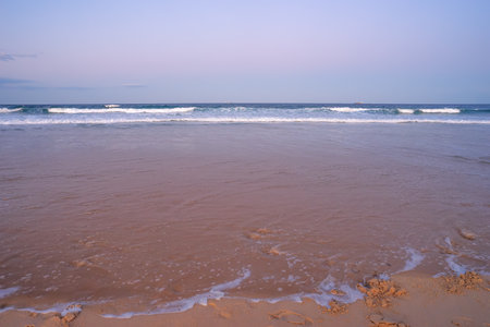 The foreshore covered by water as the tide rises on a sandy surf beach showing surf, waves, breaking...