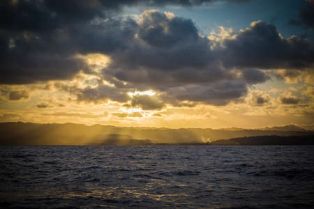 Yellow rays filter down through the clouds onto the mountains of an island in the Caribbeanの写真素材