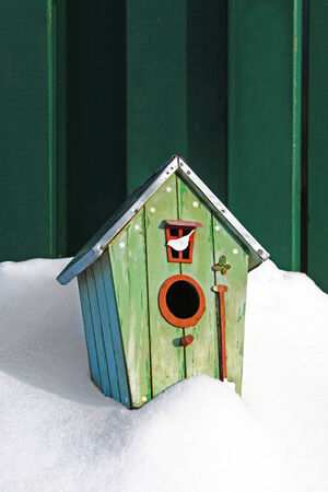 Vintage styled birdhouse in thick snow cover against a green fenceの写真素材