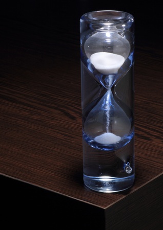 A glass blue hourglass on dark brown wooden table