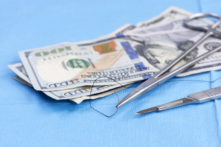 Stack of one hundred dollar bills on surgery drape with scalpel and needle holder.  Concept photo.の写真素材