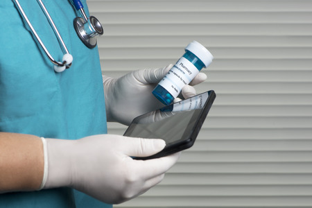 Nurse checks prescription bottle using tablet computer.の写真素材