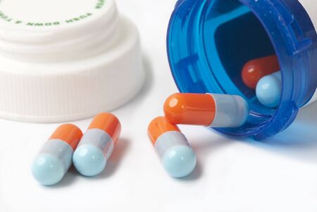 Blue and orange capsules with blue medicine bottle on white.の写真素材