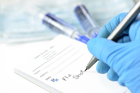 Doctor's gloved hand writes prescription for Influenza vaccine on prescription pad.