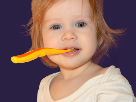 A little girl learns to brush her first milk teeth. Short-eyed Baby Girl holds her toothbrush with her teeth, looks straight and smiles at her prank.の写真素材