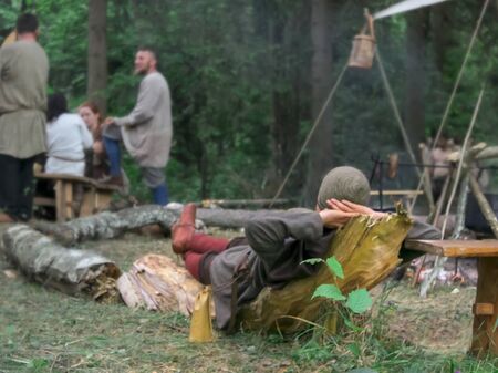 Grodek, POLAND - JULY 13, 2019. Game for adults in life of the early Middle Ages. People in historical costumes sit near bonfire and relax. Nomads on halt in forest.のeditorial素材