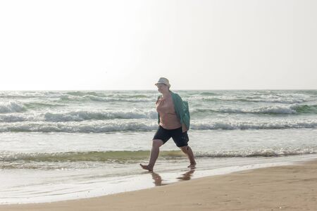 A large girl walks along the edge of the water. A woman enjoys the fresh air and the sea. The girl walks near the sea waves.の写真素材