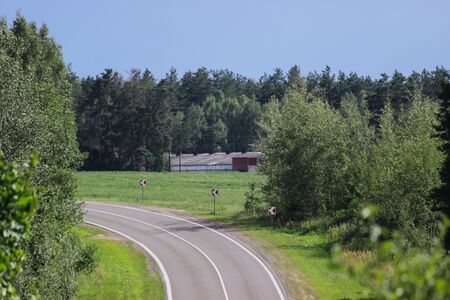 View of an empty road going uphill. Dangerous stretch of road with a turn and a climb. Rural roadway among fields and forests.の写真素材