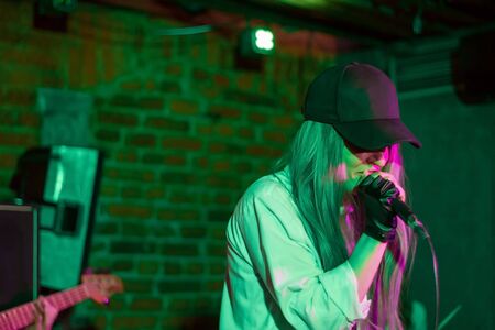 Young pretty girl in a cap sings in a rock club. Young music band in a night club. Music for the soul.の写真素材