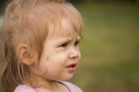 Portrait of a baby girl close-up. The child's face is smeared with sand.の写真素材
