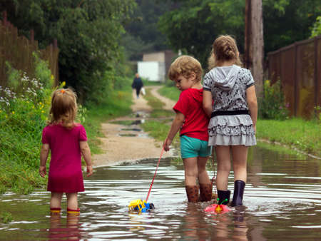 BEREZINO, BELARUS - AUGUST 13, 2019: three young children in rubber boots pull toys on a rope along a country sandy road with puddles after rain.のeditorial素材