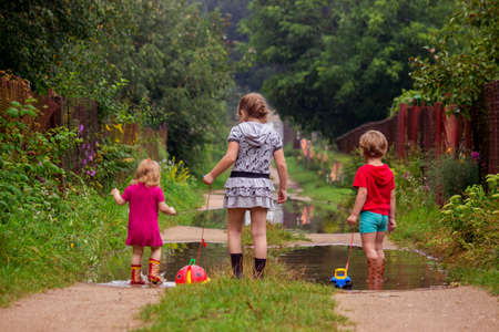 BEREZINO, BELARUS - AUGUST 13, 2019: three young children in rubber boots pull toys on a rope along a country sandy road with puddles after rain.のeditorial素材
