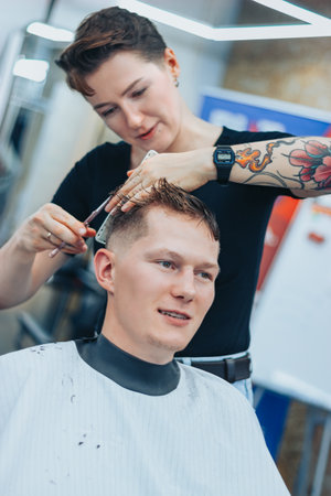 MINSK, BELARUS - OCTOBER 14, 2020: A tattooed woman hairdresser cuts guys hairのeditorial素材