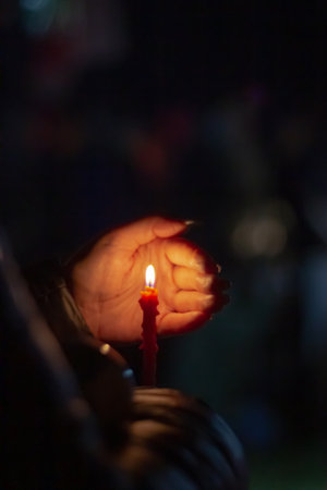 A woman holds a candle in her hand, covering the flame from the wind with her palm, in memory of the dead, killed, dead, deceased, repressed people under the open sky in the night.の素材 [FY310165769031]