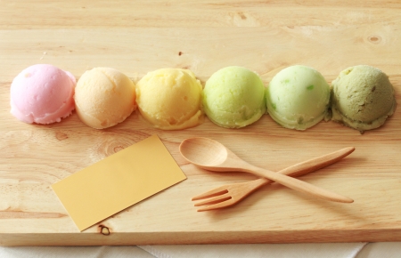 six colorful ice cream scoops in a row with spoon, fork and black cardの写真素材