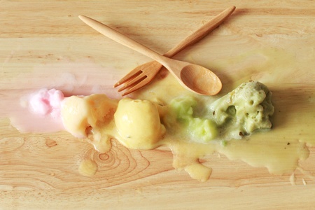 melting colorful ice cream scoops in a row with spoon and forkの写真素材