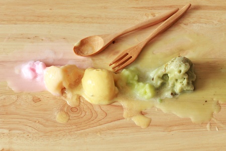 melting colorful ice cream scoops in a row with spoon and forkの写真素材