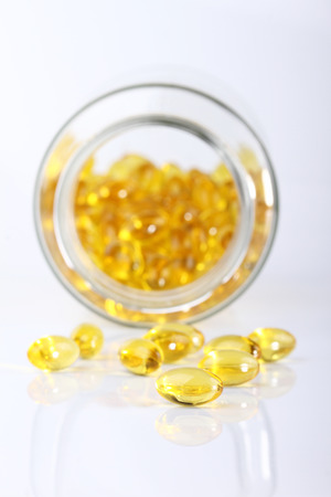 Macro view of vitamin D capsules on white with bottle in backgroundの写真素材