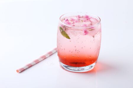 Ice cubes with pink flowers in glass  with paper straw on white backgroundの写真素材