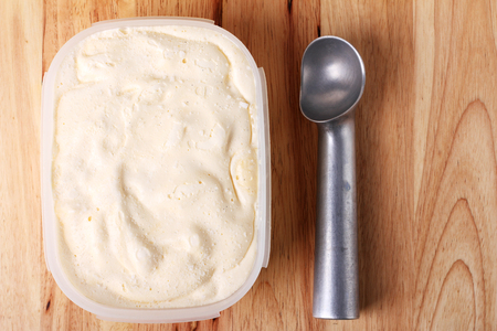 homemade creamy vanilla ice cream in a white cup container with a special spoon for scoopingの写真素材