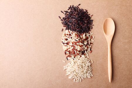 long grain rice,brown rice, with wooden spoon on brown backgroundの写真素材