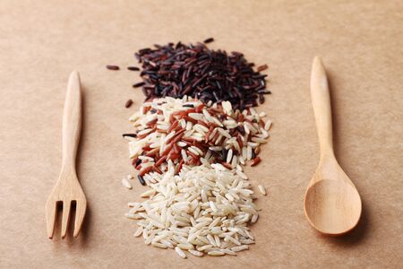 long grain rice,brown rice, with wooden spoon and fork on brown backgroundの写真素材