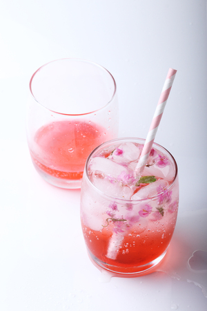 Ice cubes with pink flowers in glass  with paper straw on white backgroundの写真素材