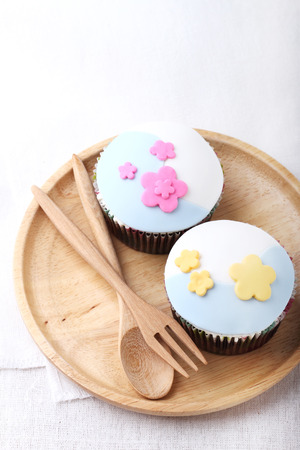 two chocolate cupcakes decorate with flower pastel color fondant on wooden plateの写真素材