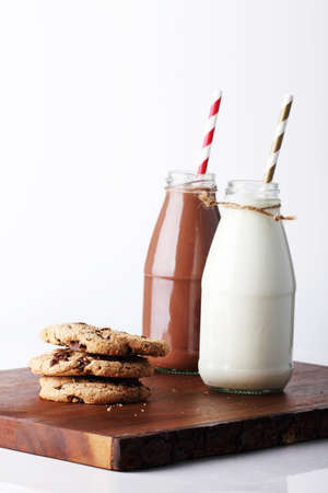 retro bottles of milk with striped straw and cookies on wooden boardの写真素材