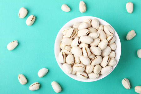 Pistachio nuts in white ceramic bowl on color backgroundの写真素材