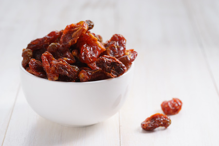 Delicious dried tomatoes in bowl on white wooden background.の写真素材