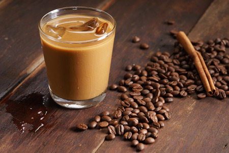 glass of iced coffee with milk on wooden table with coffee beansの写真素材