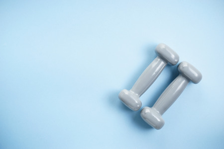 two gray dumbbells on light blue background, fitness and healthy concept