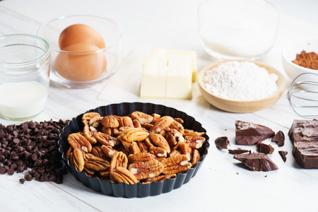 baking ingredients with chocolate and pecan nut for sweet pastry on white wooden tableの写真素材