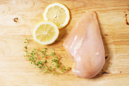Raw chicken breast fillet, lemon and thyme on wooden board, cooking ingredientsの写真素材