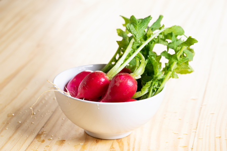 Bunch of fresh small radish in white bowl on wooden tableの写真素材
