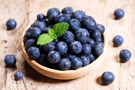 Fresh blueberries in wooden bowl with mint leaves on rustic wooden