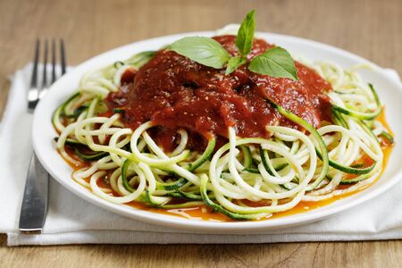 zucchini pasta with tomato sauce in white plate on wooden tableの写真素材